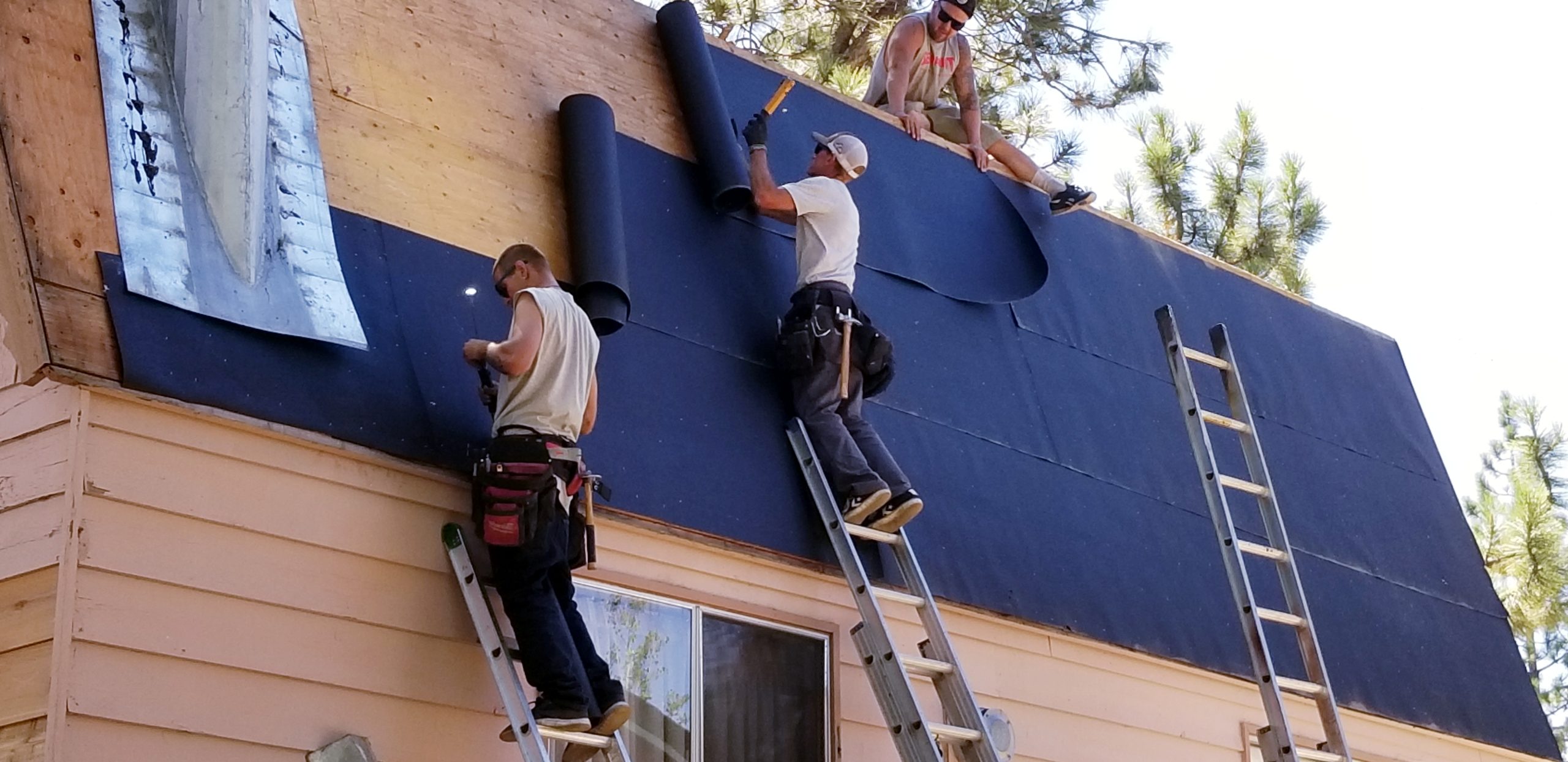 3 Men on Side of Roof Nailing Down Black Fabric